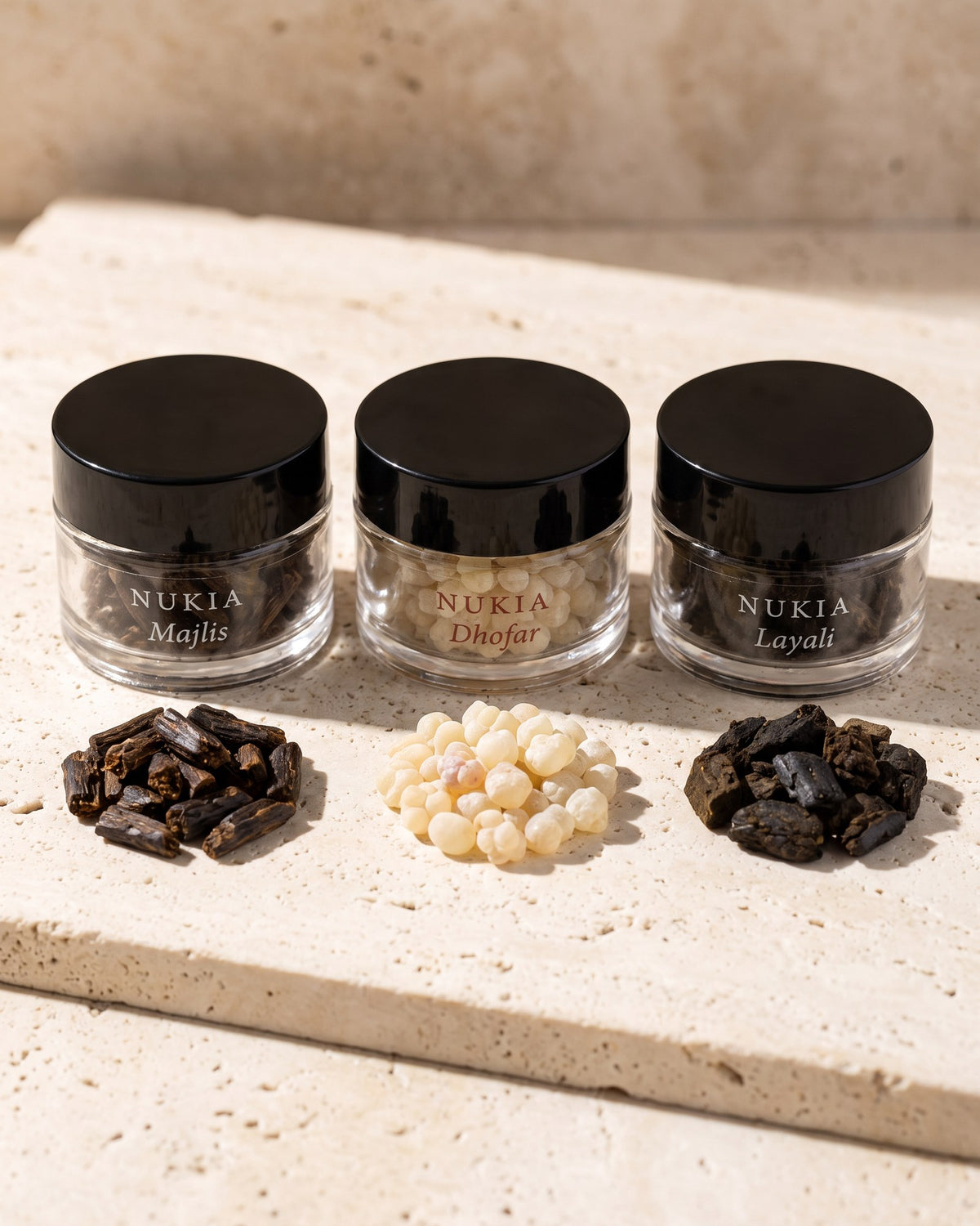 Three jars with bakhoor chips and frankincense pearls on travertine